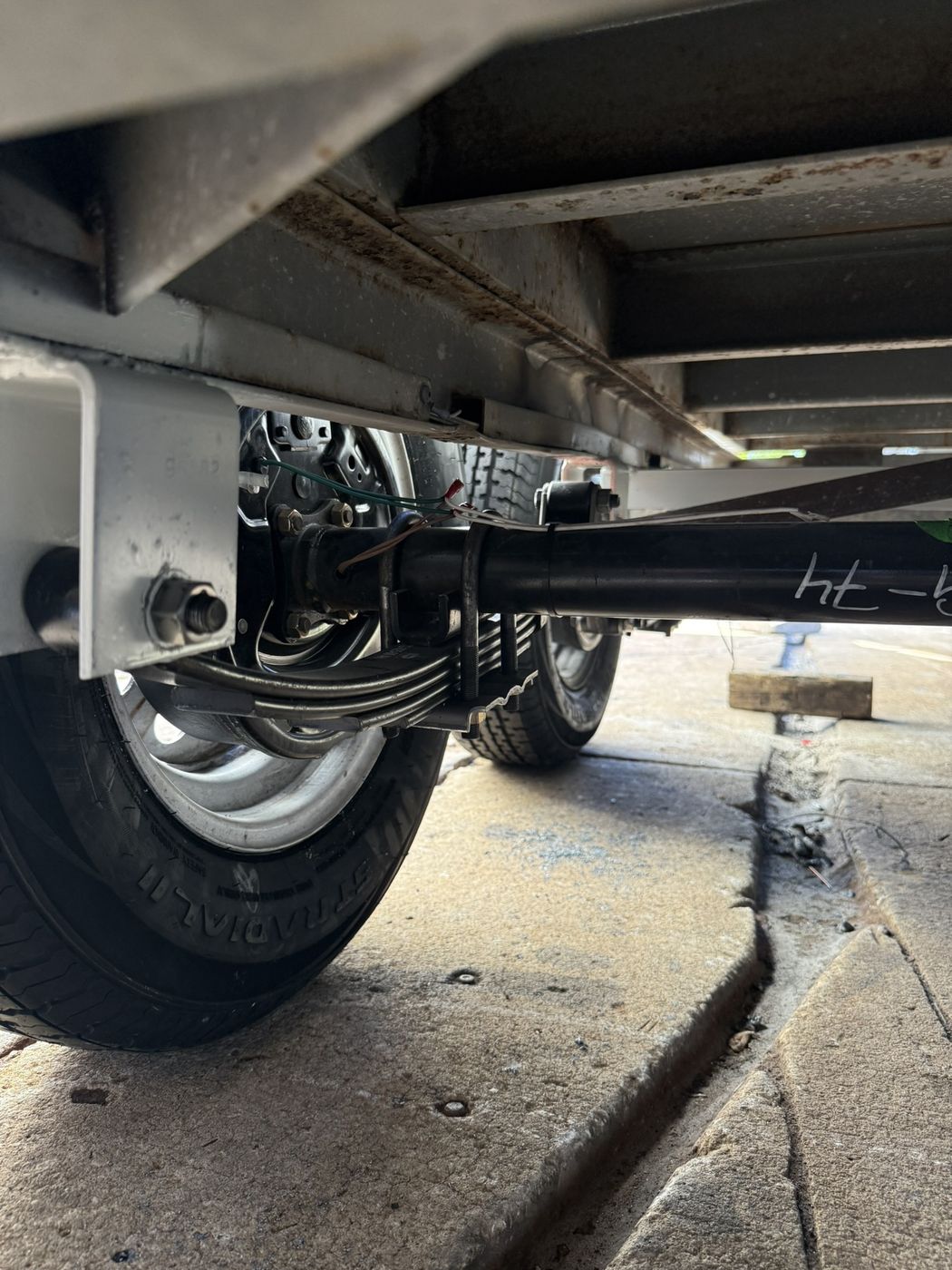 Trailer axle with leaf springs and new tire seen from underneath